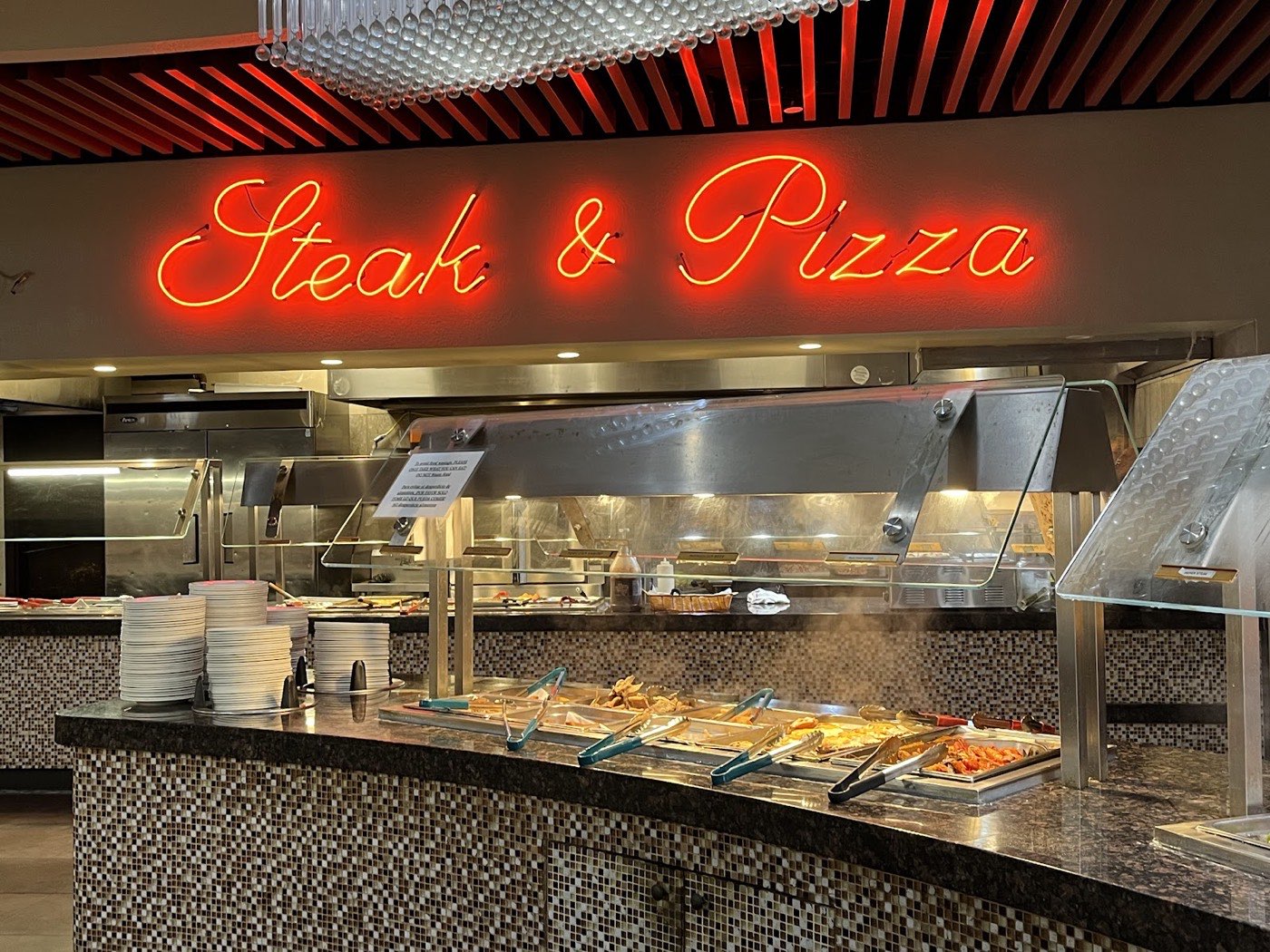 Steak and pizza station under a red neon sign at Kin's Chinese Buffet